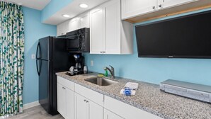 Una cucina con mobili bianchi, un frigorifero nero, un forno a microonde, una macchina da caffè, un lavandino e una TV a schermo piatto.