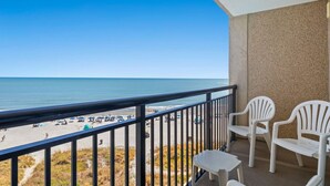 Un balcone con vista sulla spiaggia e sull'oceano. Si notano due sedie di plastica bianca e un tavolino.