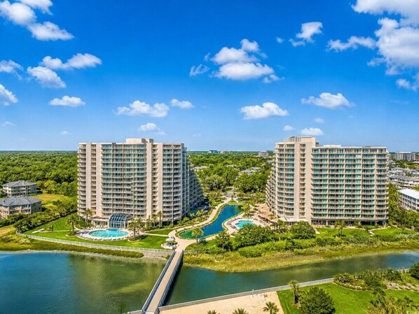 A high-rise hotel with multiple floors, a swimming pool, and a bridge connecting to a body of water.