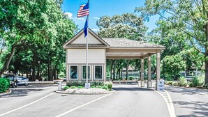 A covered building with a flagpole, a paved entrance, and a landscaped area with trees and shrubs. - Oceanfront Resort Condo with Relaxing Pool Hot Tub (Myrtle Beach)