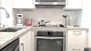 A modern kitchen with white cabinets, a stainless steel microwave, a coffee maker, and a stove. - Oceanfront Resort Condo with Relaxing Pool Hot Tub (Myrtle Beach)