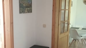 Una habitación con piso de madera, un reposapiés negro, un cuadro en la pared y una puerta que da a otra habitación.