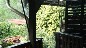 Un espacio exterior cubierto con suelo de baldosas, barandillas de madera y vistas a zonas verdes y un edificio con tejado rojo.
