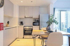 Cozinha moderna com fogão, forno, micro-ondas e geladeira. Há uma mesa de jantar com cadeiras e um vaso com plantas.