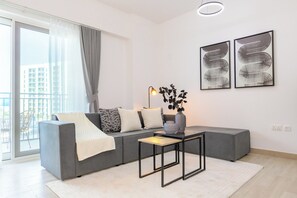 Uma sala de estar moderna com um sofá seccional cinza, uma pequena mesa preta e duas pinturas abstratas na parede.
