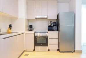 Cozinha compacta equipada com forno embutido, cafeteira, micro-ondas e frigorífico.