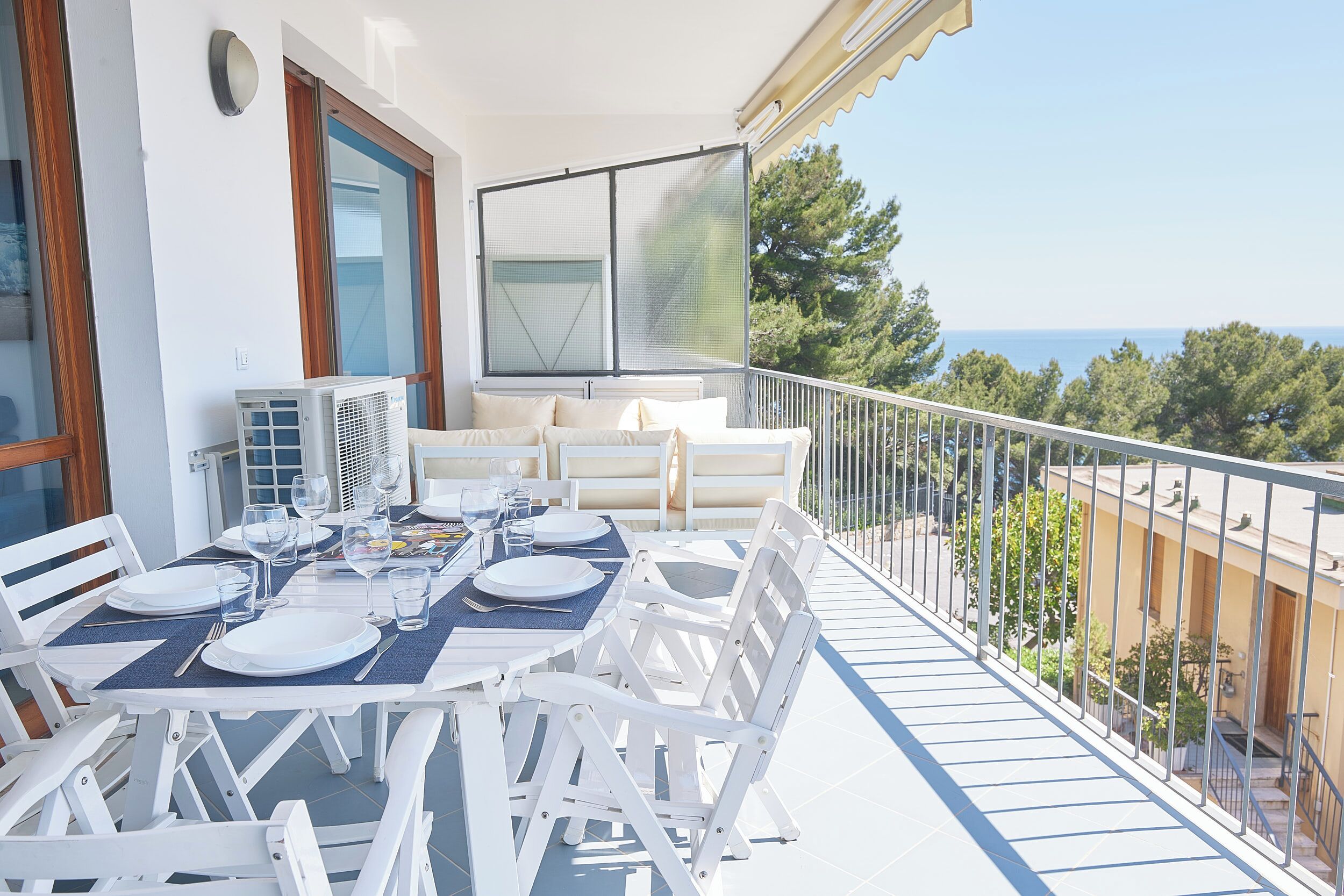 Ein Balkon mit Esstisch, weißen Gartenmöbeln und Blick aufs Meer.