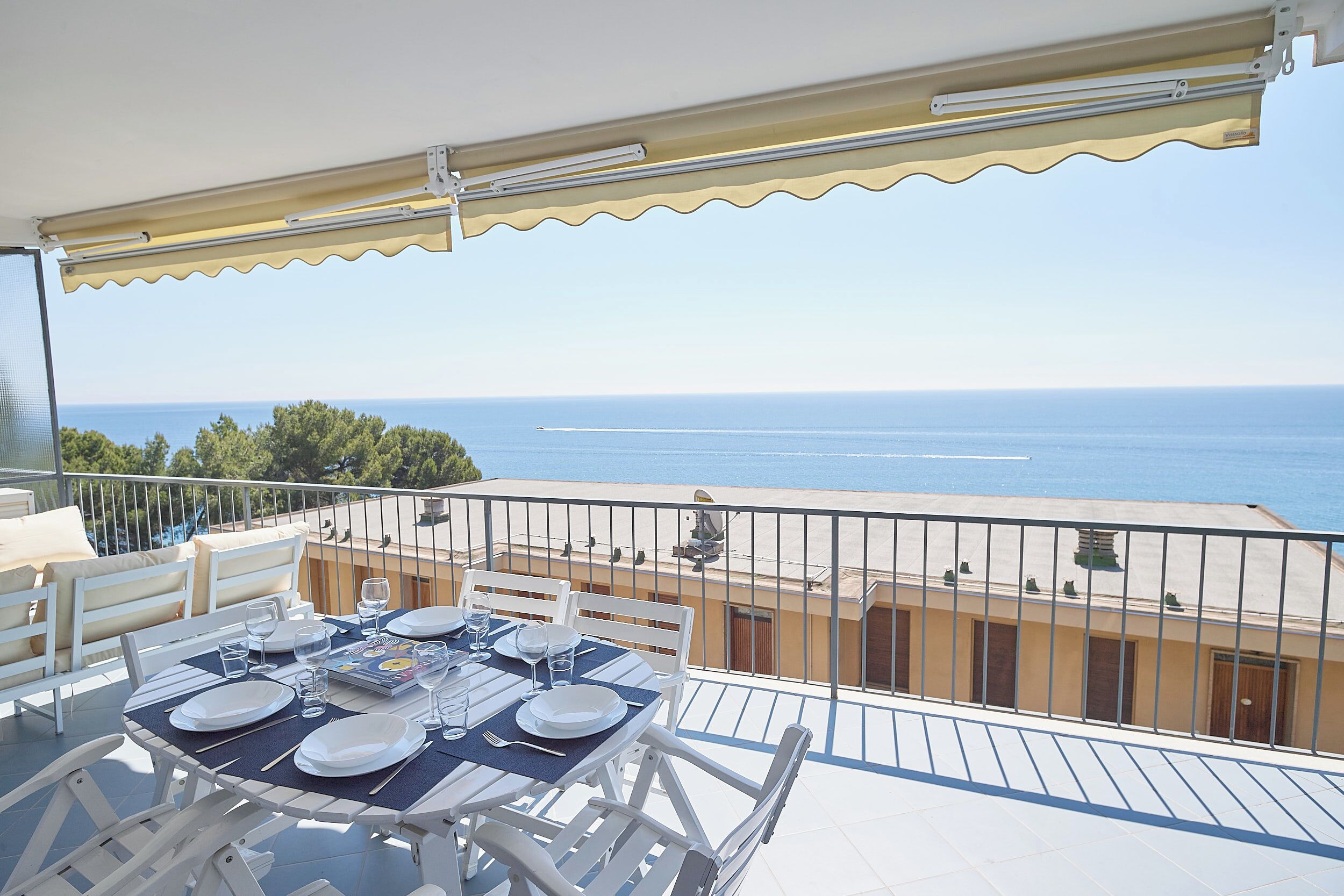 Un balcón con mesa lista para comer, con vista al mar.