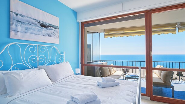 A bedroom with a large bed, a view of the ocean, and a balcony with outdoor seating. - I Gabbiani sul Mare (Cervo)