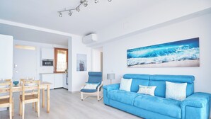 A modern living room with a blue sofa, wooden dining table, and chairs. - I Gabbiani sul Mare (Cervo)