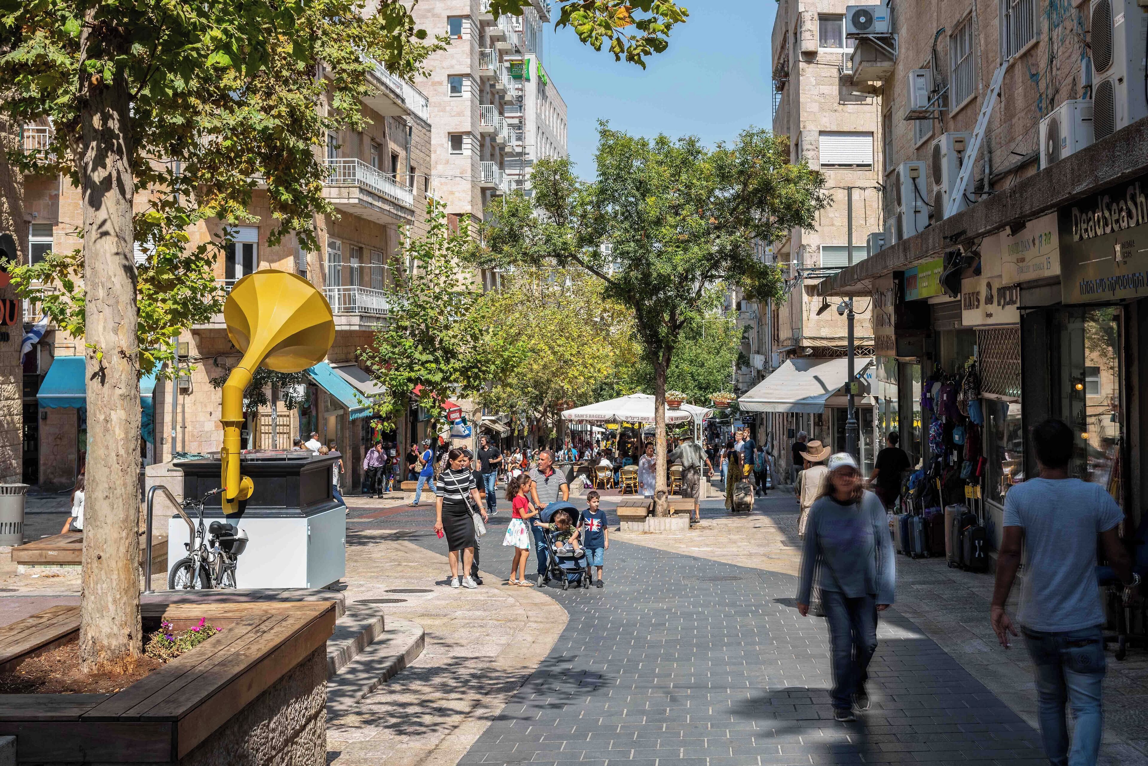 Una calle urbana concurrida con peatones, una escultura amarilla y edificios de varios pisos.