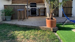 En udendørs terrasse med grill, træterrasse og krukker med planter.