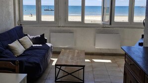 Une pièce dotée d’une grande fenêtre donnant sur une plage, d’un canapé bleu foncé, d’une petite table en bois et d’un meuble.