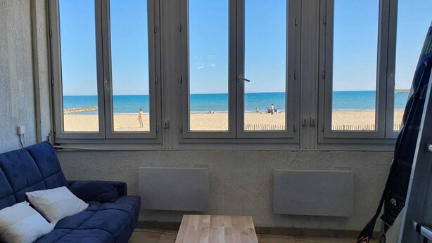 Une pièce avec un canapé bleu, une table en bois et de grandes fenêtres donnant sur une plage.