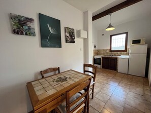 Compact kitchen with a dining area, featuring a refrigerator, microwave, and stove, as well as a dining table with a tablecloth and chairs.