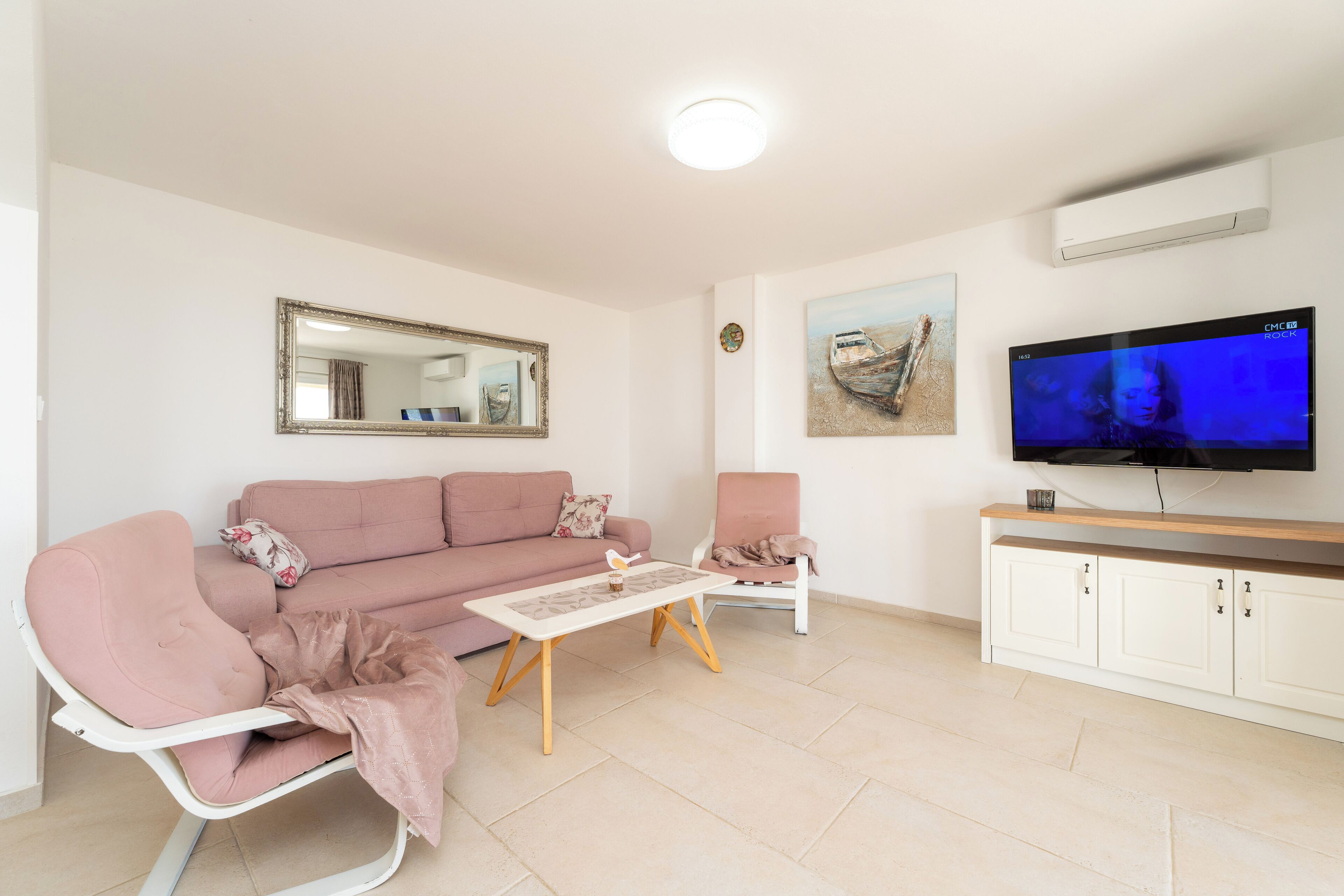 Una sala de estar con un sofá rosa, una mesa de centro, un televisor, un espejo y un armario.