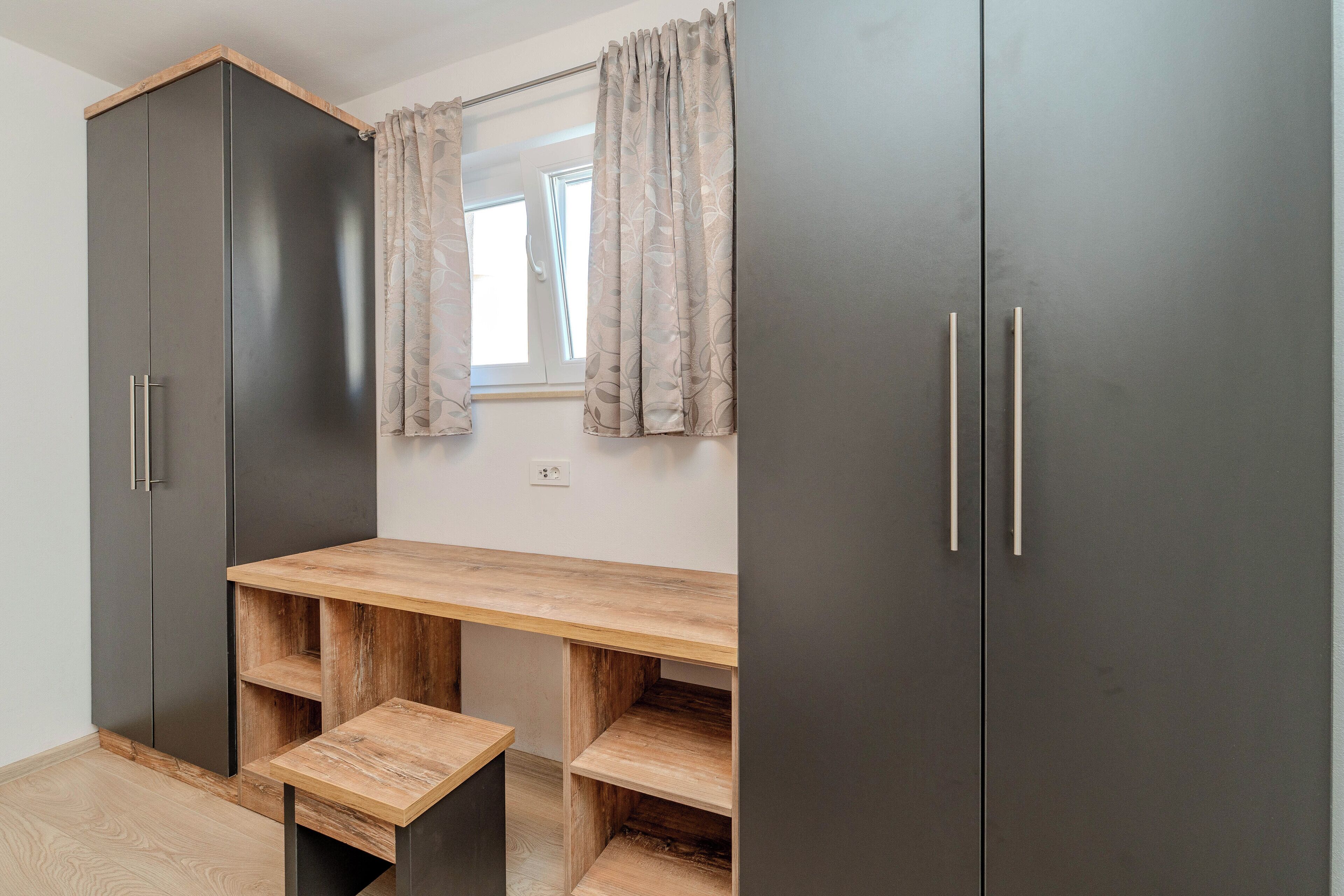A room with a wooden desk, two black cabinets, and a window with curtains.