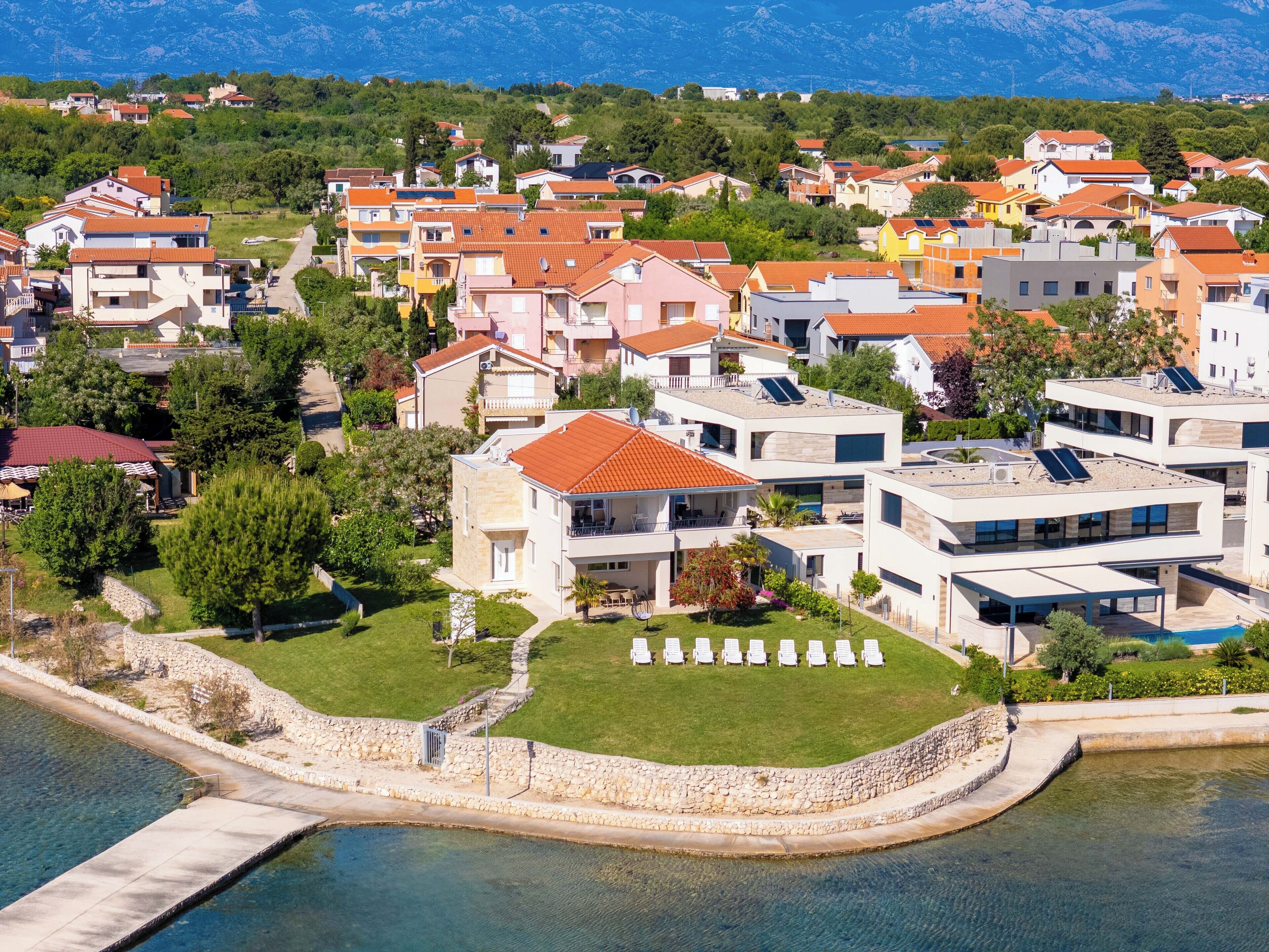 A coastal residential area with modern houses, a swimming pool, and a stone wall.