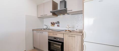 Cocina compacta con horno integrado, microondas y campana extractora de acero inoxidable.