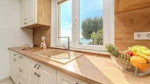 A modern kitchen with white cabinets, a wooden countertop, a large window, and a fruit bowl on the counter. - Apartments Batela  (Privlaka)