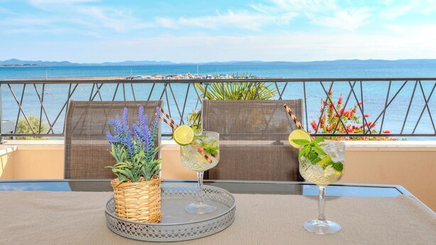 A table with two drinks, a wicker basket with plants, and a view of the sea. - Apartments Batela  (Privlaka)