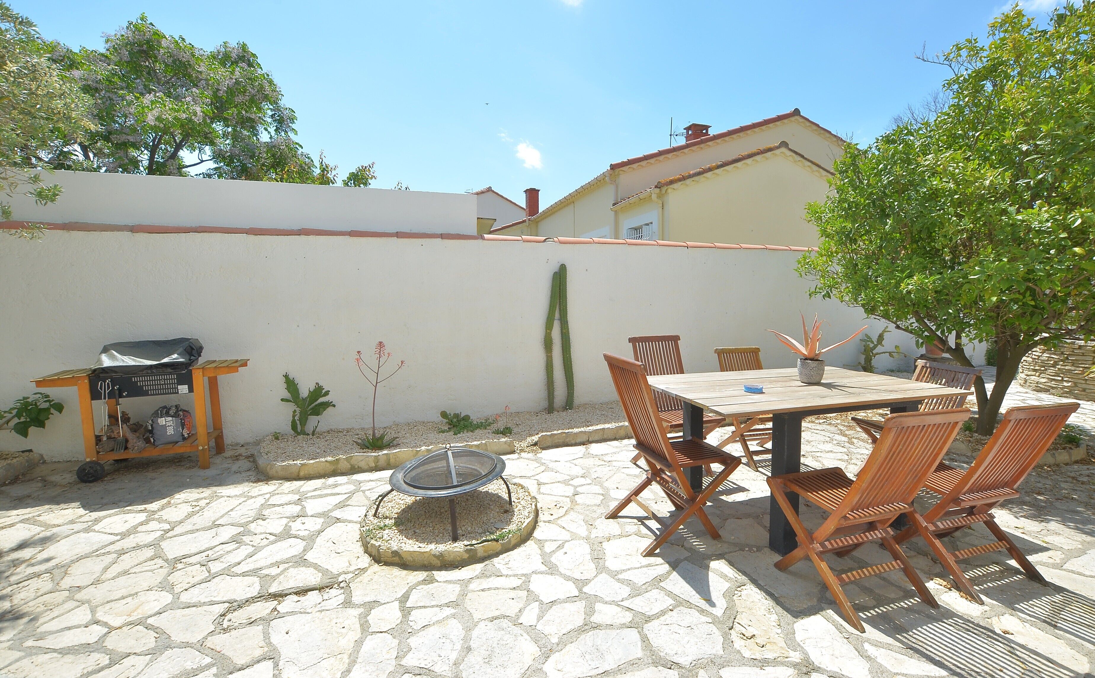 An outdoor patio with a stone floor, a table with chairs, a fire pit, and a cactus plant.