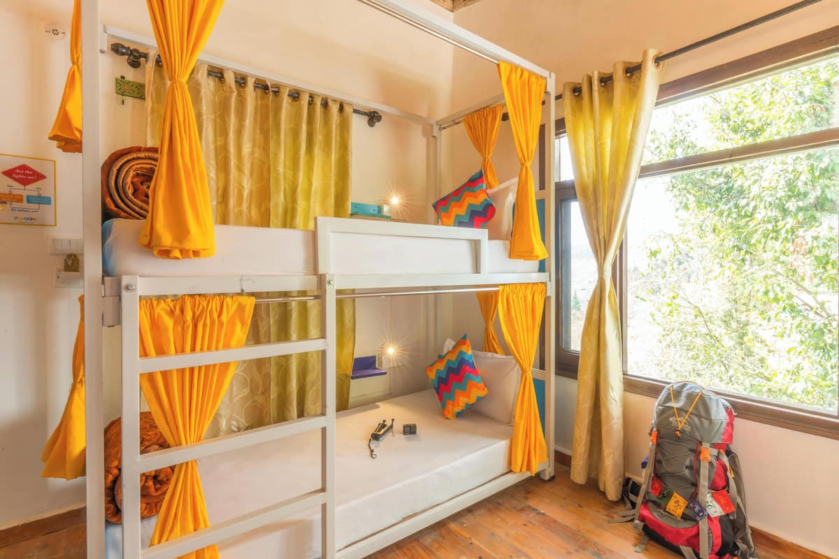 A bunk bed room with yellow curtains, a window with a view of trees, and a backpack on the floor.