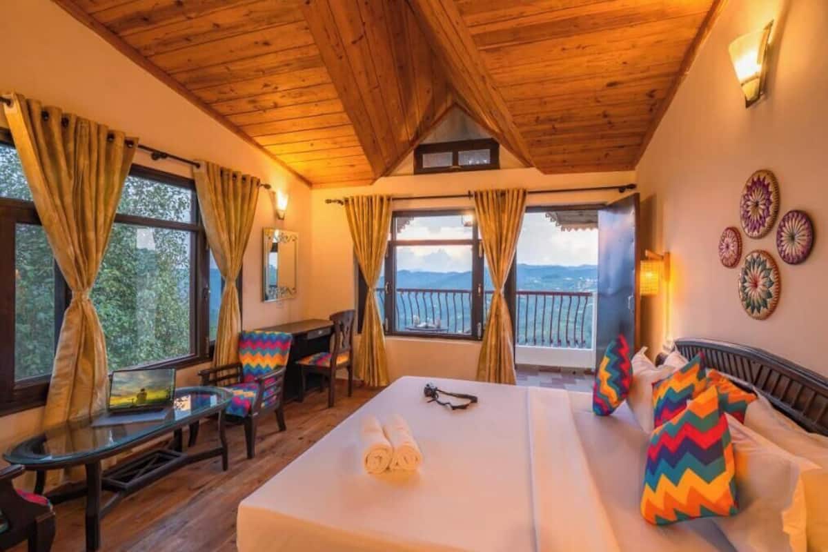 A room with a bed, a desk, and a chair, with large windows and a balcony.