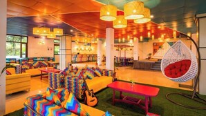 A vibrant lounge area with colorful zigzag-patterned sofas, a hanging chair with a red cushion, and a red table.