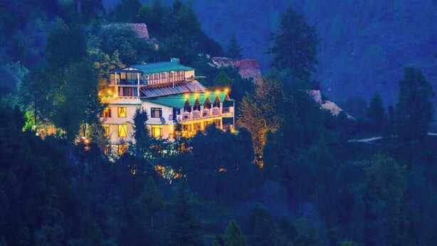 A multi-story building with balconies, surrounded by dense forest.