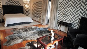 A bedroom with a large bed, a chandelier, a fur rug, a piano, and chevron-patterned wallpaper. - Casa Puebla - Cangas de Onís (Cangas de Onís)