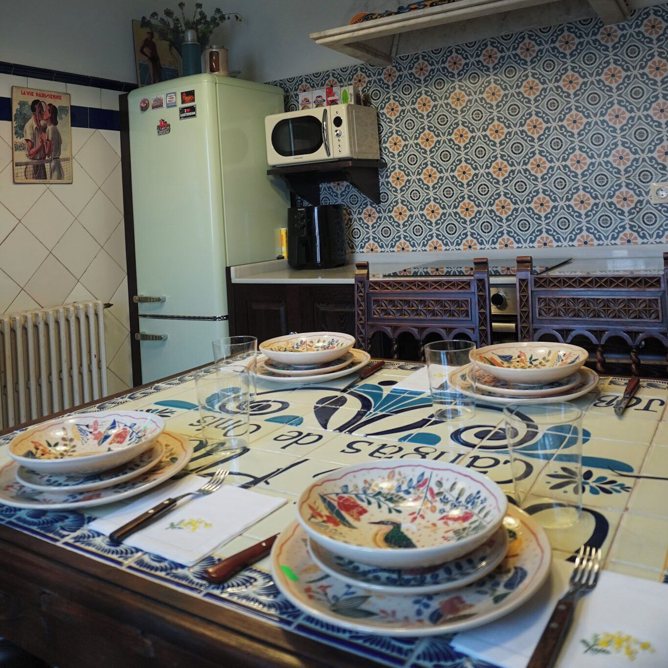 A dining table set with plates, bowls, and cutlery, a refrigerator, a microwave, and a tiled backsplash.