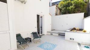 A patio with two lounge chairs, a patterned floor design, and a small garden area with plants. - Via Roma Suites (Ischia)