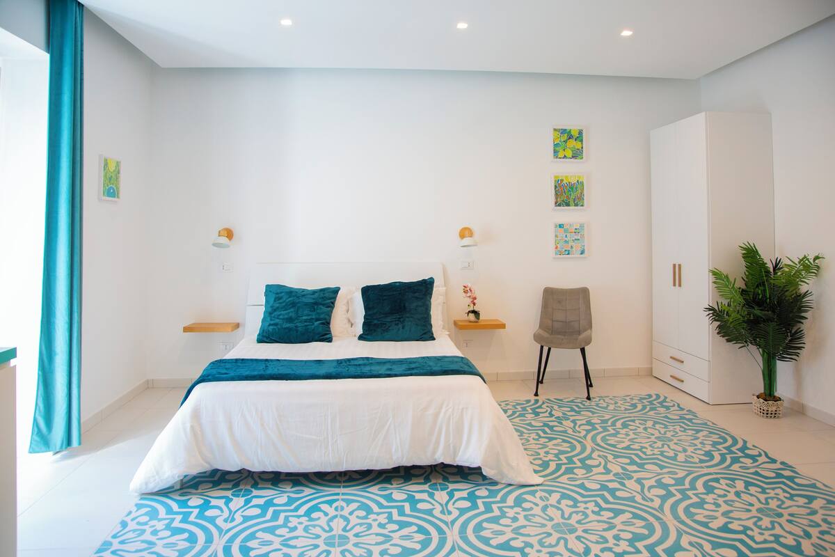A modern bedroom with a large bed, a wardrobe, a chair, and a potted plant.