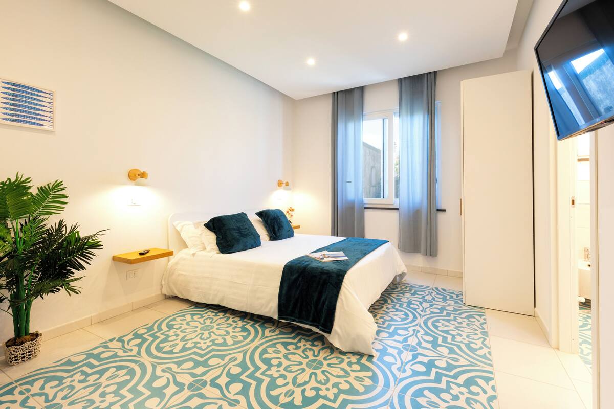 A modern bedroom with a large bed, a potted plant, and a patterned floor.