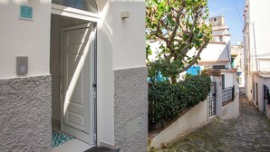A narrow cobblestone street with a white building featuring a door and a small step leading to the entrance. - Via Roma Suites (Ischia)