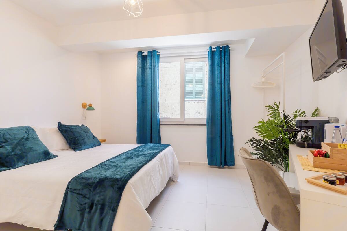 A hotel room with a bed, a desk, a chair, a TV, and a window with curtains.