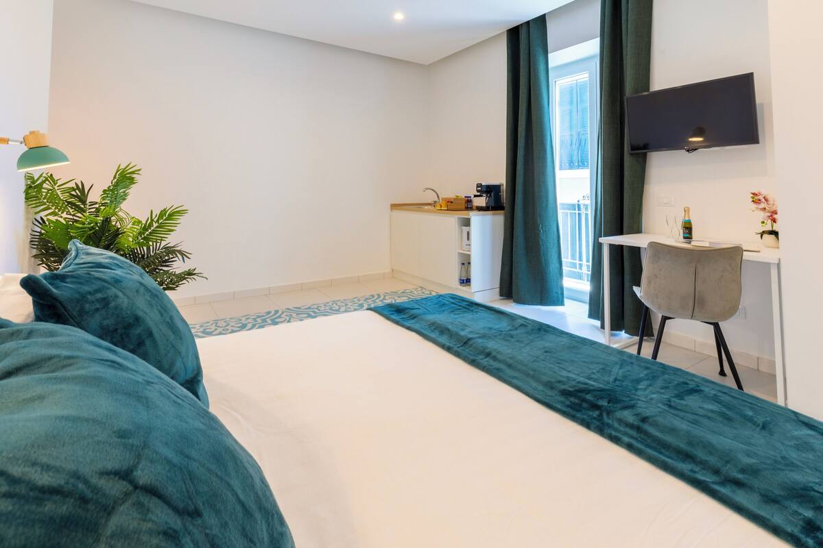 A modern hotel room with a large bed, a desk with a chair, a TV, and a view of the outdoors.