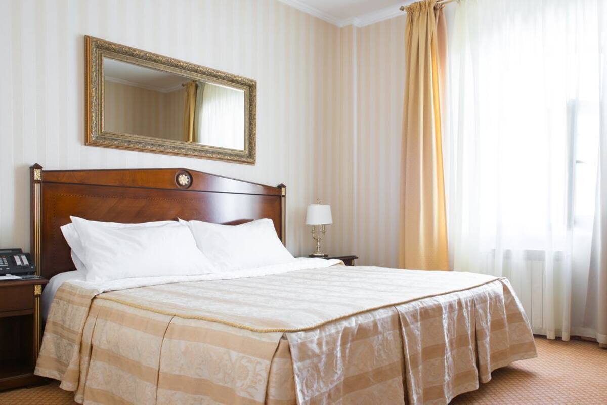 Una habitación de hotel con una cama grande, una mesita de noche, una lámpara, un teléfono, un espejo y una ventana con cortinas.