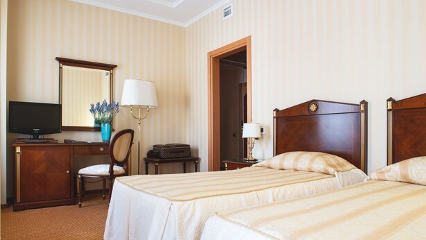 A hotel room with two beds, a desk with a television, a chair, a lamp, and a mirror. - Optima Collection Podil Plaza (Kyiv)
