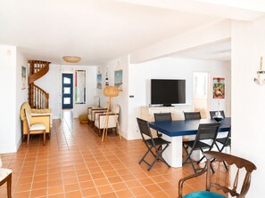 A spacious living area with a dining table, chairs, a TV, and a staircase.