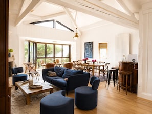 A spacious living room with a high ceiling, large windows, a dining area, and a modern kitchen.