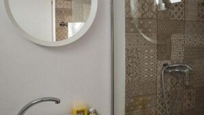 A bathroom with a round mirror, a shower with a glass door, and patterned tiles. - The Moon Villas (Vama Veche)