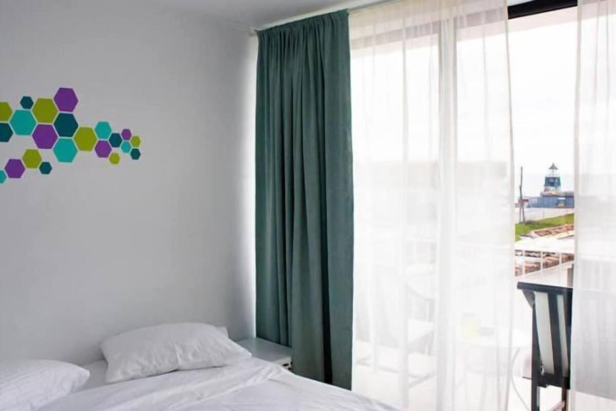 Habitación de hotel con cama, vista a un edificio a través de cortinas translúcidas y decoración de pared con forma de hexágonos.