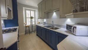 Una cocina moderna con estufa a gas, microondas y pileta. Hay una ventana con vista al exterior, y una silla colocada cerca de la ventana.