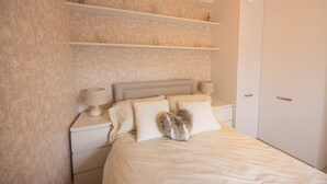 Un dormitorio con cama, mesitas de noche, lámpara y estante en la pared.