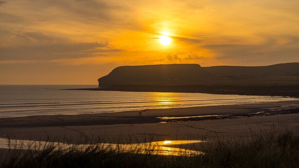 Un atardecer sobre una playa con un acantilado al fondo.