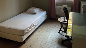 A small, single-bed room with a wooden floor, a window with curtains, a desk with a chair, and two framed pictures on the wall. - Lodging for the 24h of Le Mans week in the historic city center. (Le Mans)