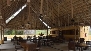 Un espace de restauration en plein air avec des tables et des chaises en bois, un toit de chaume et des ventilateurs de plafond.
