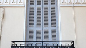Fachada de edificio con ventanal con contraventanas verticales, barandilla decorativa y diseño arquitectónico clásico.